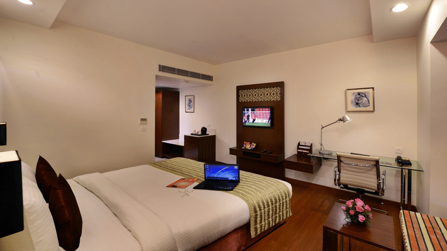 A double bed with laptop on it, TV, work desk, hallway to bathroom