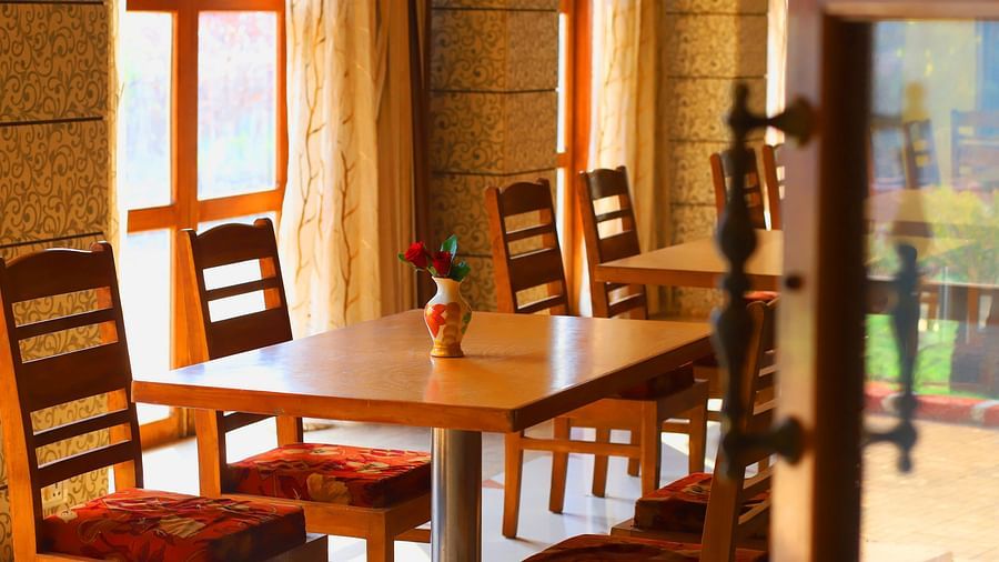 Dining area with wooden tables and cushioned chairs, warm lighting, and a single flower vase at Hotel Kohinoor Highway, Dapoli