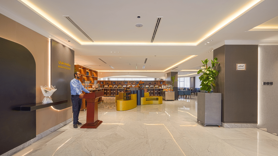 The Nahraan Restaurant welcoming desk seen with a staff member in uniform awaiting a guests' arrival at the restaurant, with the dining tables set in the background under bright lighting.