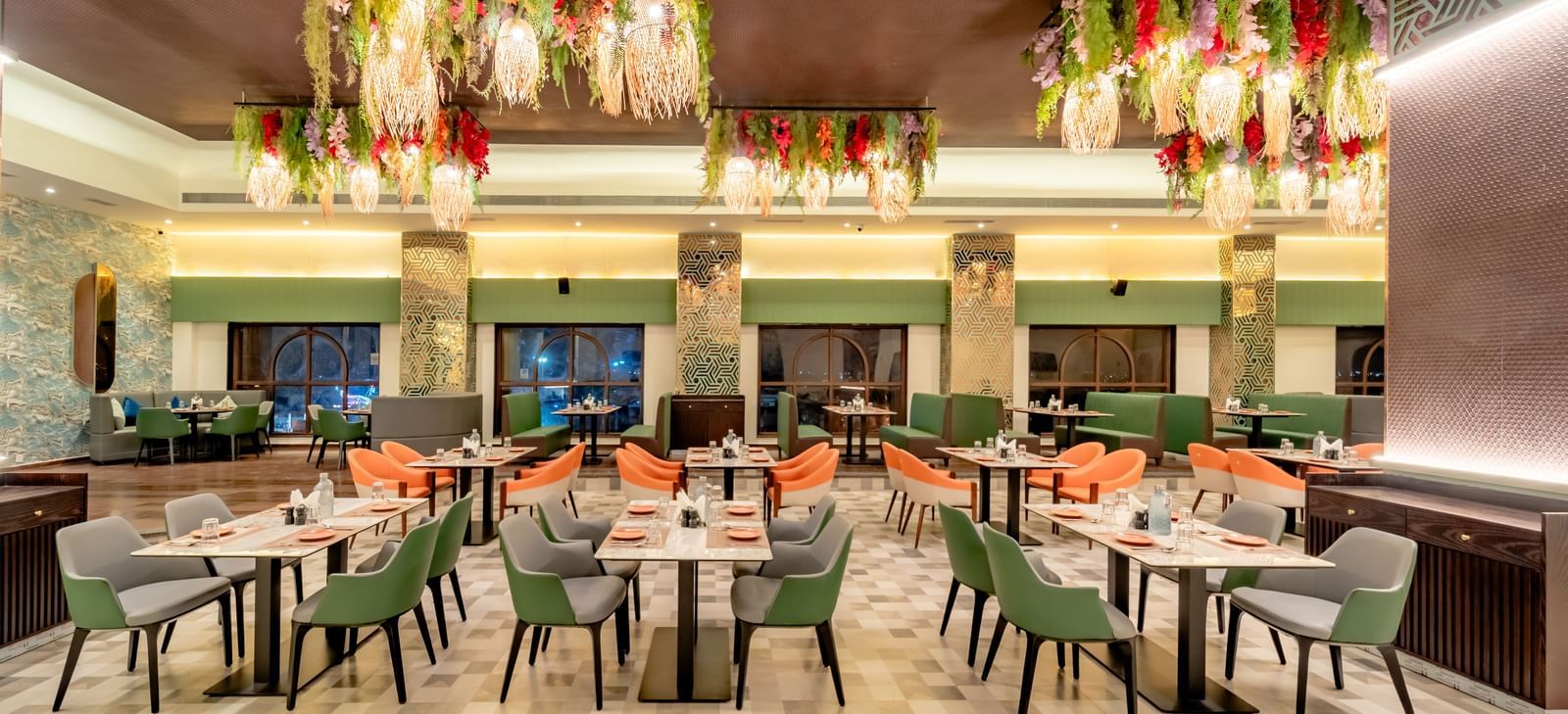 Dining area with green and orange chairs and decorative hanging lights and elements | Pravasa Hotel, Vijayapura