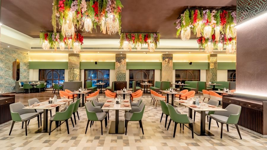 Dining area with green and orange chairs and decorative hanging lights and elements | Pravasa Hotel, Vijayapura
