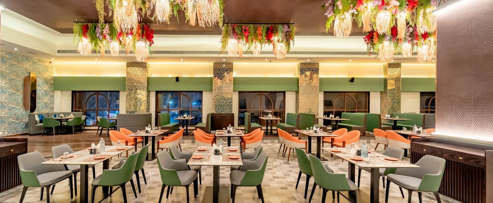 Dining area with green and orange chairs and decorative hanging lights and elements | Pravasa Hotel, Vijayapura