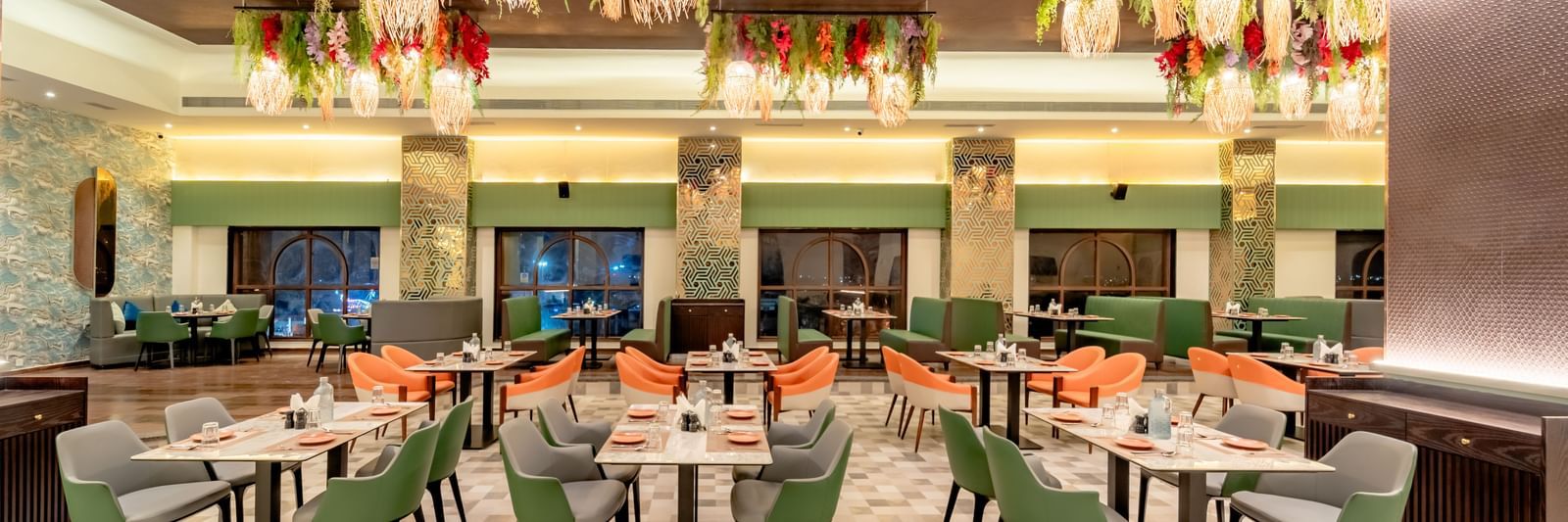 Dining area with green and orange chairs and decorative hanging lights and elements | Pravasa Hotel, Vijayapura