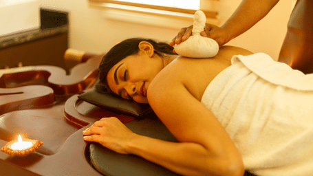 A person receiving a shoulder massage with a poultice while lying on a massage table.