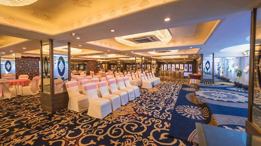 Magadh setup with rows of chairs and tables, featuring ornate carpeting and ceiling lights.