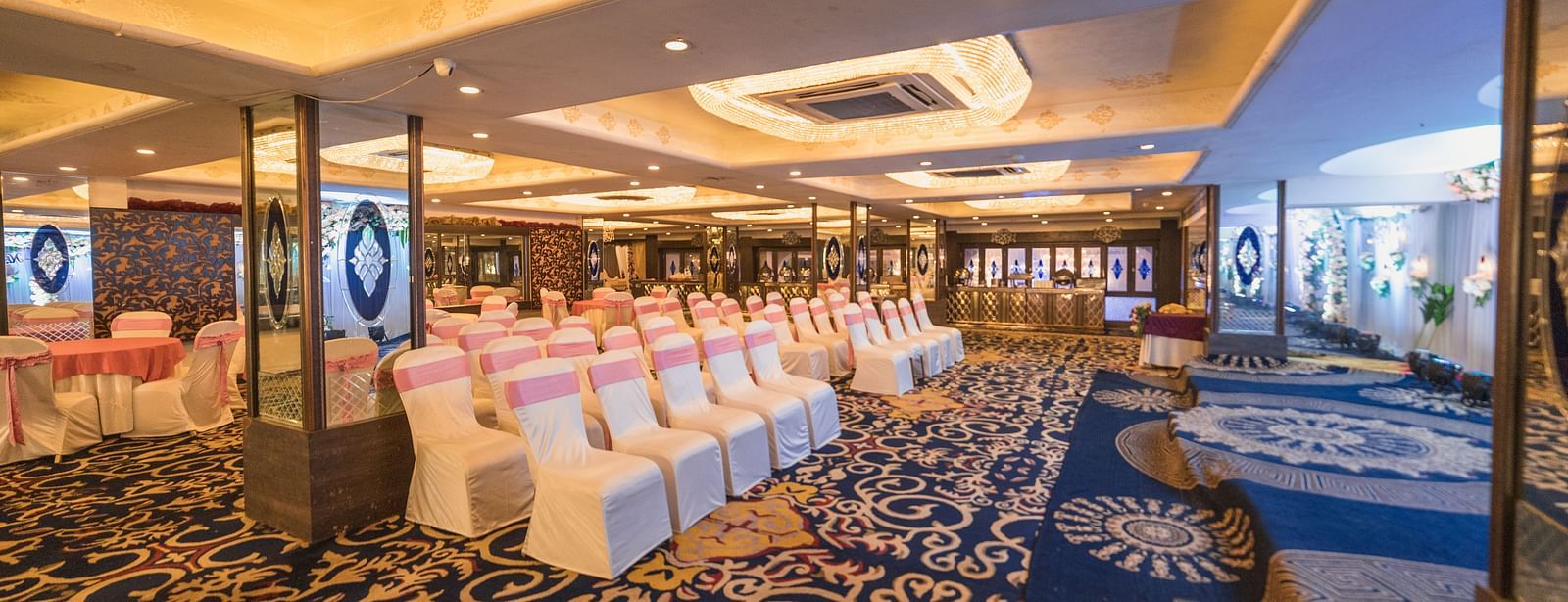 Magadh setup with rows of chairs and tables, featuring ornate carpeting and ceiling lights.