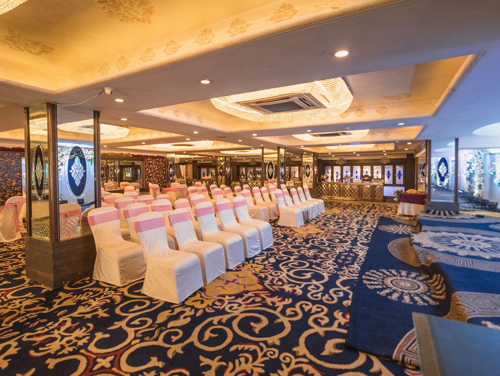 Magadh setup with rows of chairs and tables, featuring ornate carpeting and ceiling lights.