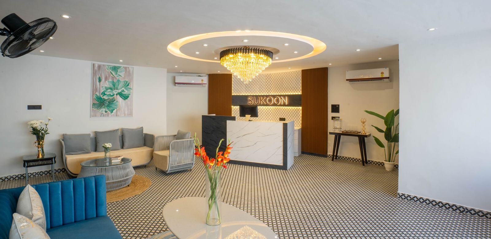 The stylish lobby of Sukoon by the Ganges features plush blue sofas, contemporary decor, and a striking central chandelier.