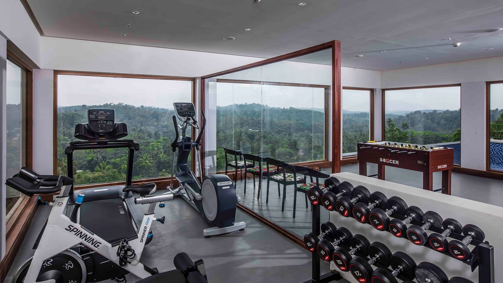 A image of the gym at our hotel with all equipment and glass windows overlooking the mountains | Great Trails Wayanad by  GRT hotels.