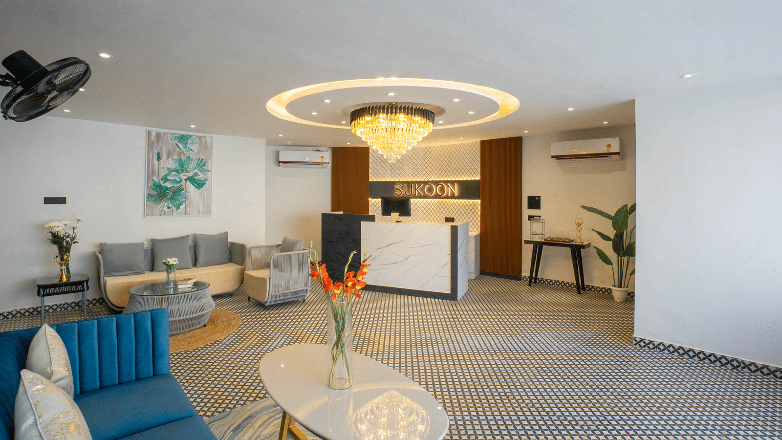 The stylish lobby of Sukoon by the Ganges features plush blue sofas, contemporary decor, and a striking central chandelier.