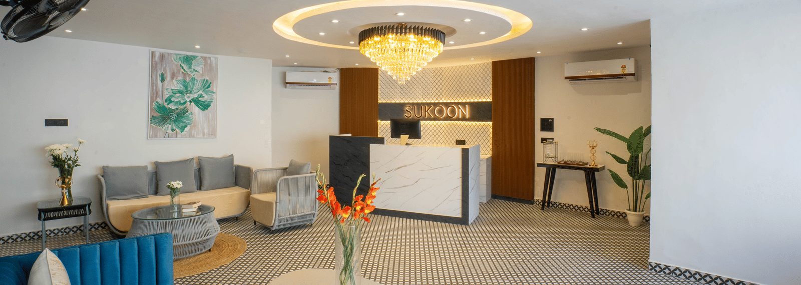 The stylish lobby of Sukoon by the Ganges features plush blue sofas, contemporary decor, and a striking central chandelier.