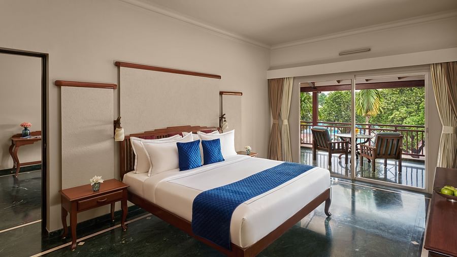 Executive Suite at DGV Resort by Treat, Silvassa with a large bed, elegant wooden furniture, and a balcony overlooking lush greenery.