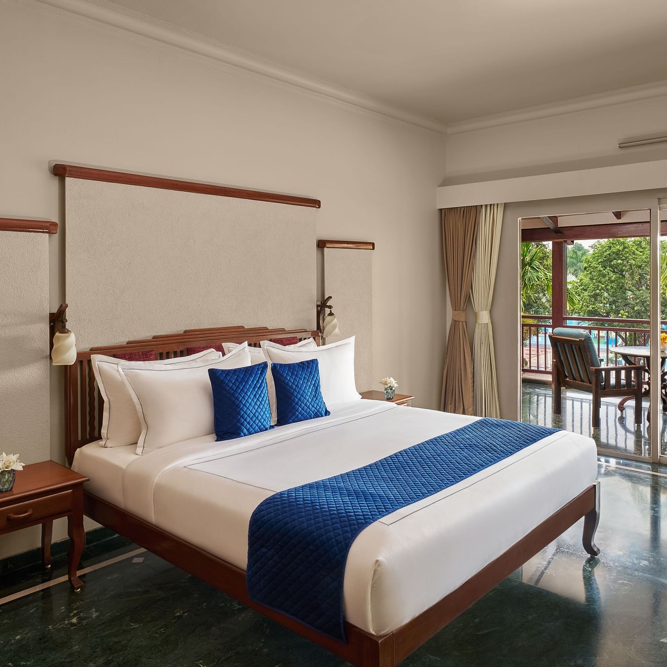 Executive Suite at DGV Resort by Treat, Silvassa with a large bed, elegant wooden furniture, and a balcony overlooking lush greenery.