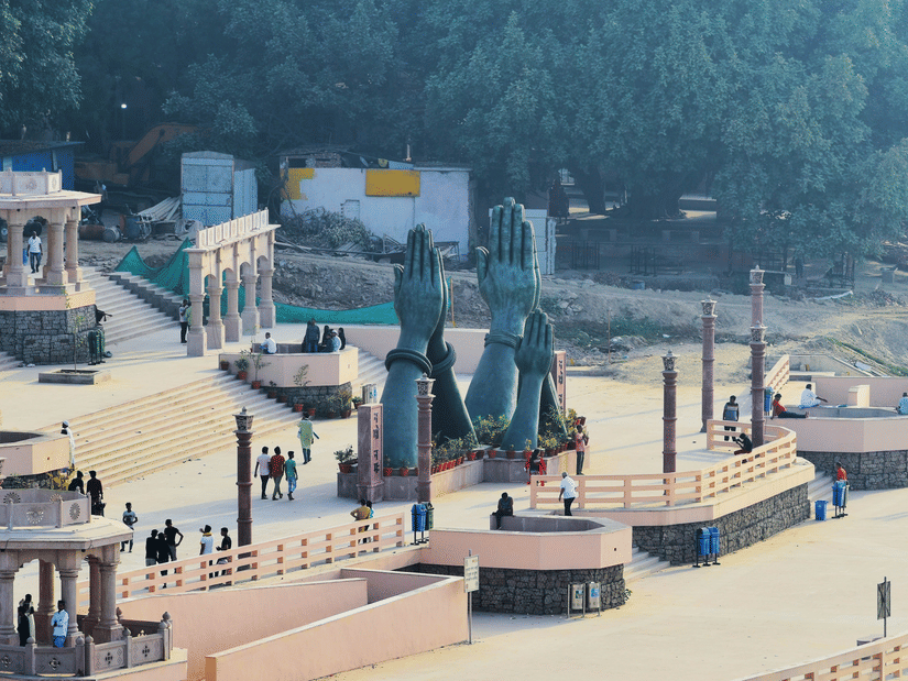 An elevated view of a stone riverfront area with small pavilions and people walking | HHI Varanasi
