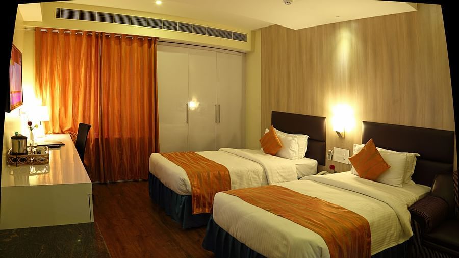 A modern hotel room features a king-sized bed with decorative pillows and a runner, bedside lighting, a window with curtains, and a wardrobe -  Renest Tirupati 
