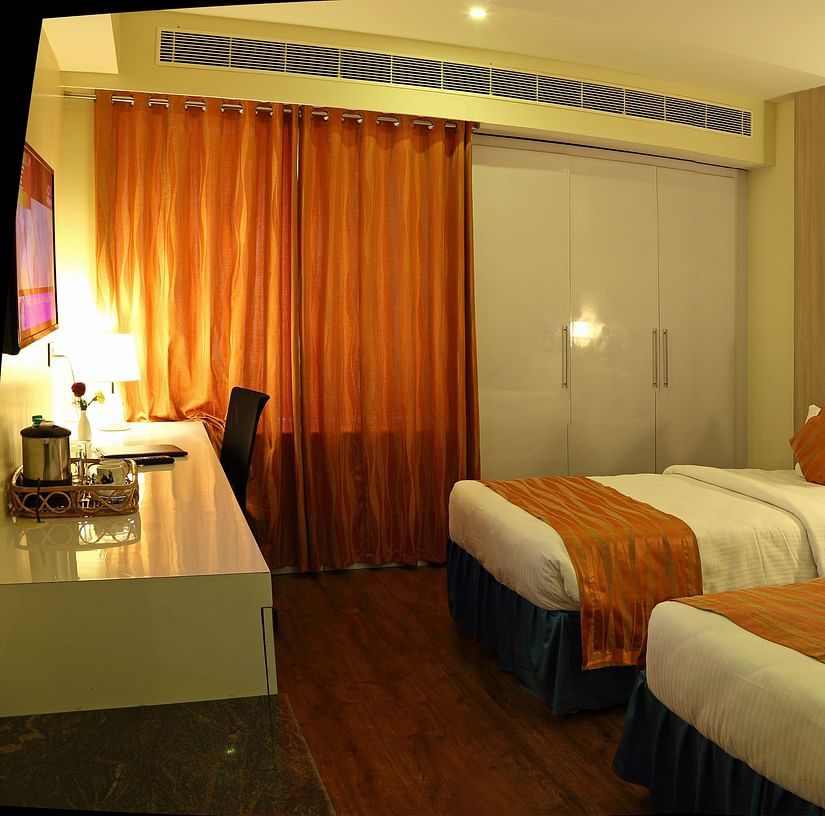 A modern hotel room features a king-sized bed with decorative pillows and a runner, bedside lighting, a window with curtains, and a wardrobe -  Renest Tirupati 
