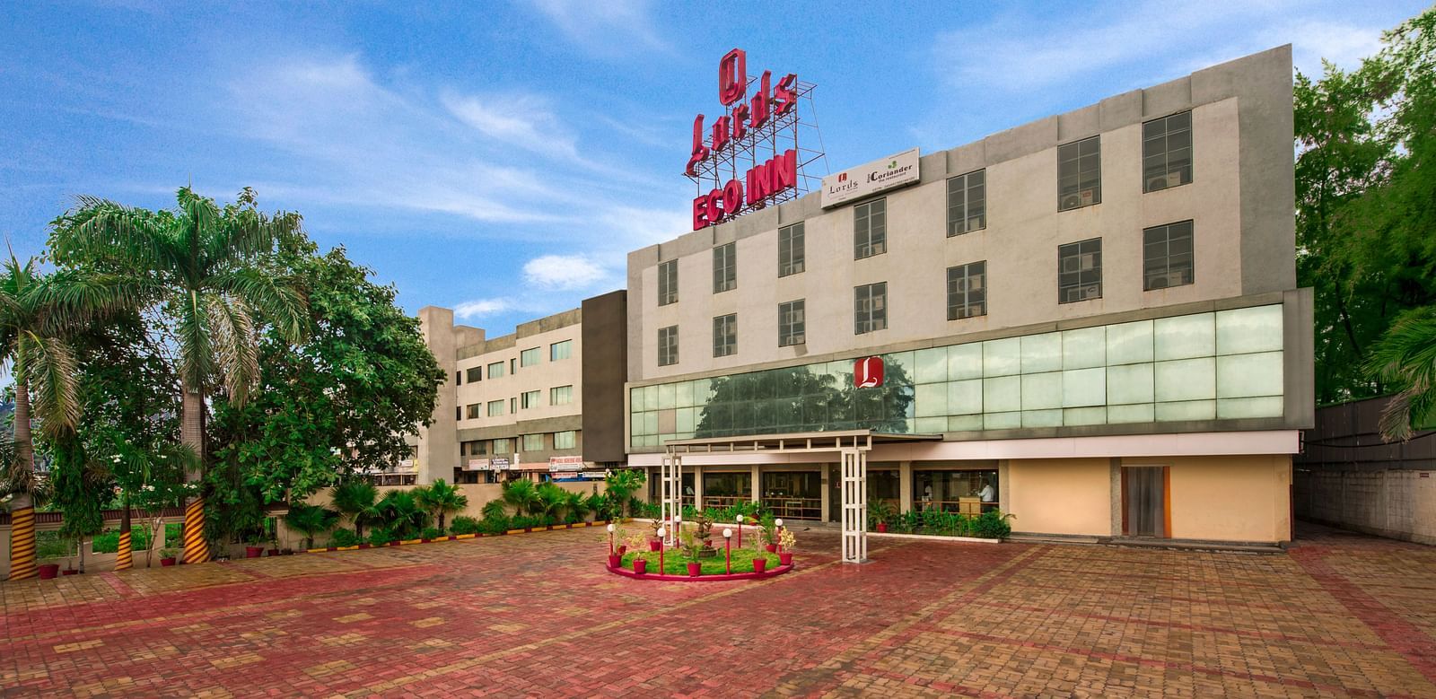 A wider exterior shot of the hotel, showing its facade and surrounding greenery - Lords Eco Inn Dahej