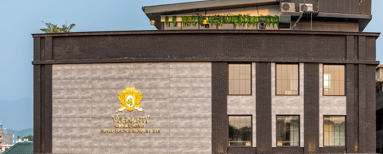 Overview shot of the facade of Vishranti Resort Dehradun showcasing its logo engraved on the wall taken during the day.