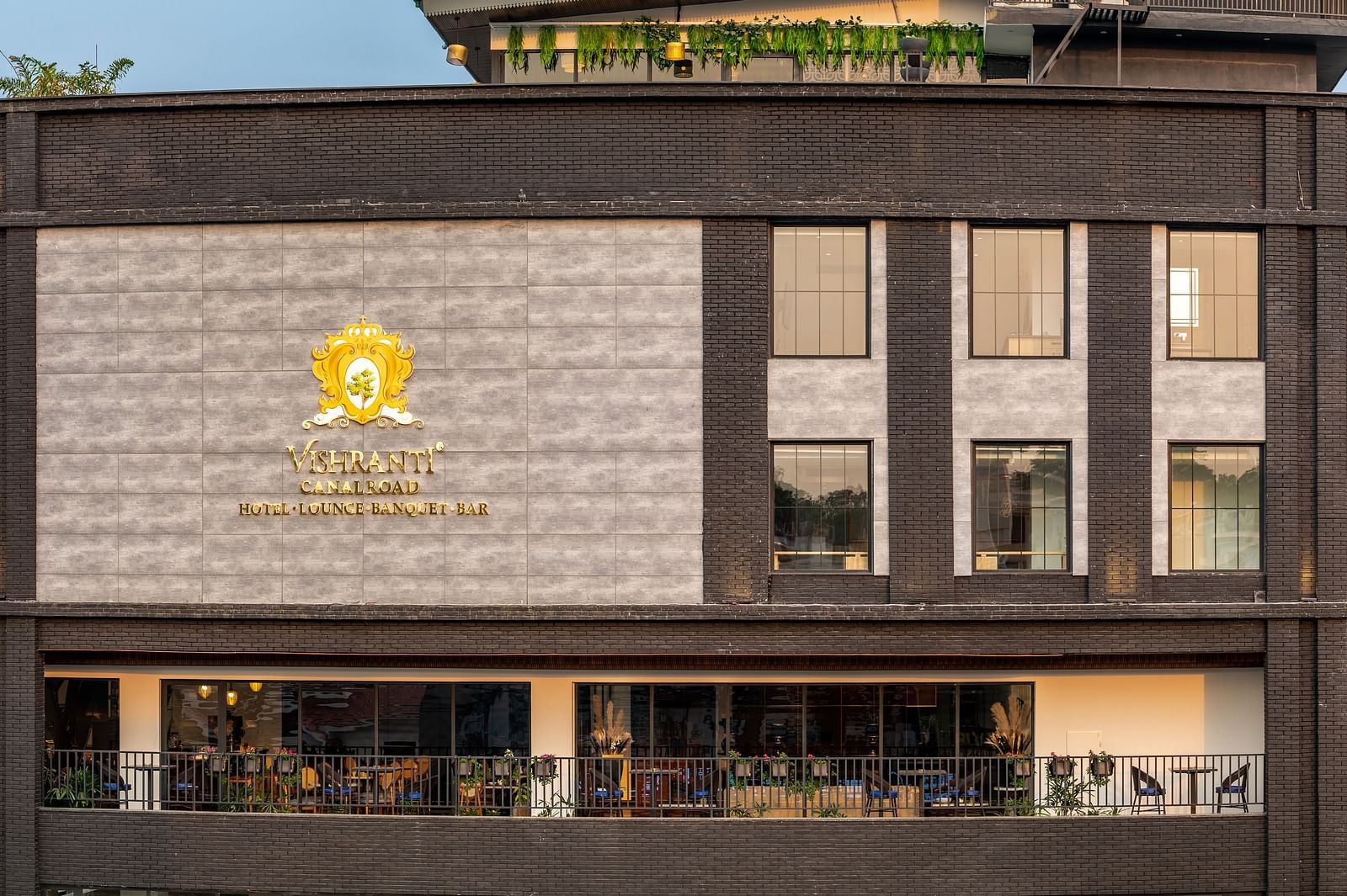 Overview shot of the facade of Vishranti Hotel Dehradun showcasing its logo engraved on the wall taken during the day.