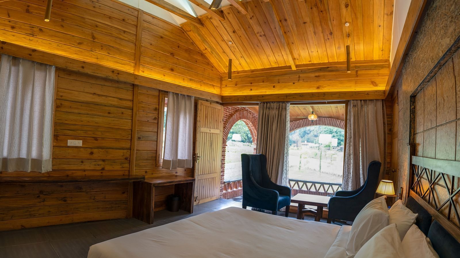 A view through a large bed placed next to chairs at Superior Room at the Sylvan Retreat, Dehradun.