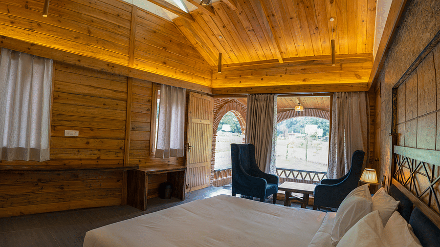 A view through a large bed placed next to chairs at Superior Room at the Sylvan Retreat, Dehradun.
