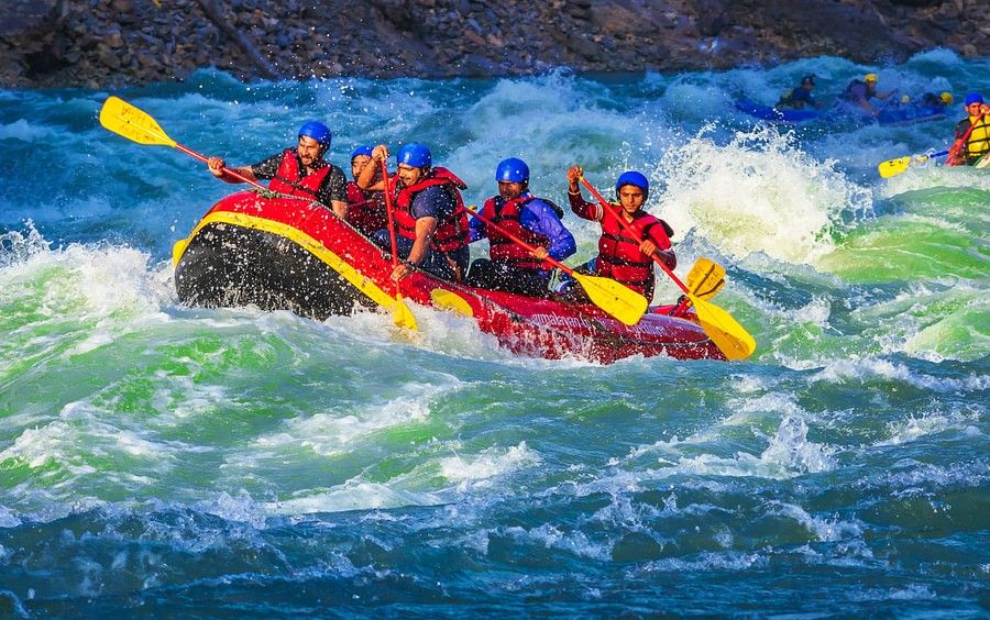 alt-text A raft filled with seven people, wearing red life jackets and helmets, is navigating through turbulent, white-capped waters. Everyone appears exhilarated by the action.