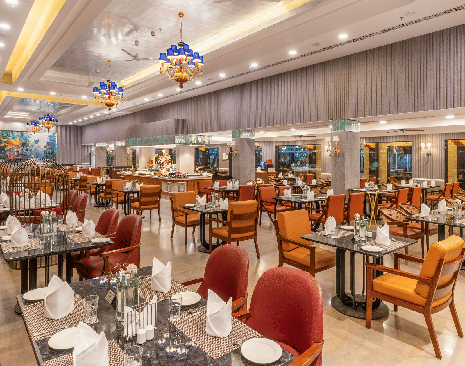 Tea Pot restaurant with marble tables, red and orange chairs, chandeliers, decorative birdcages and a buffet counter at MAYFAIR Palm Beach Resort, Gopalpur-on-Sea.