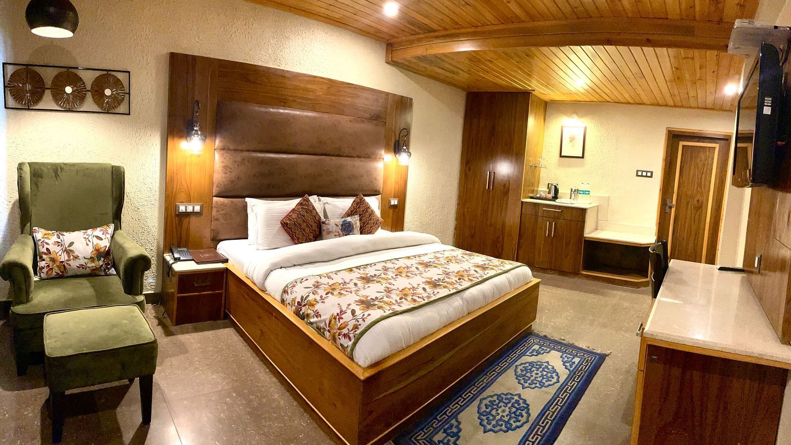 A bedroom with a plush bed, chair, TV, and a wardrobe | Mongas Hotel & Resort, Dalhousie