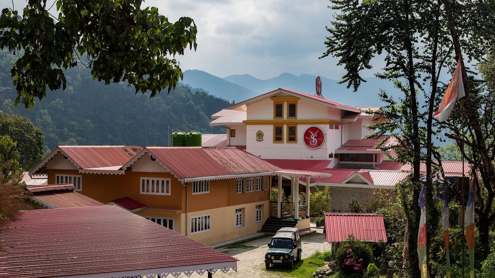 Charming hillside buildings with red rooftops set against a backdrop of lush green mountains under a partly cloudy sky - Yashshree Pelling Chekhim Retreat.