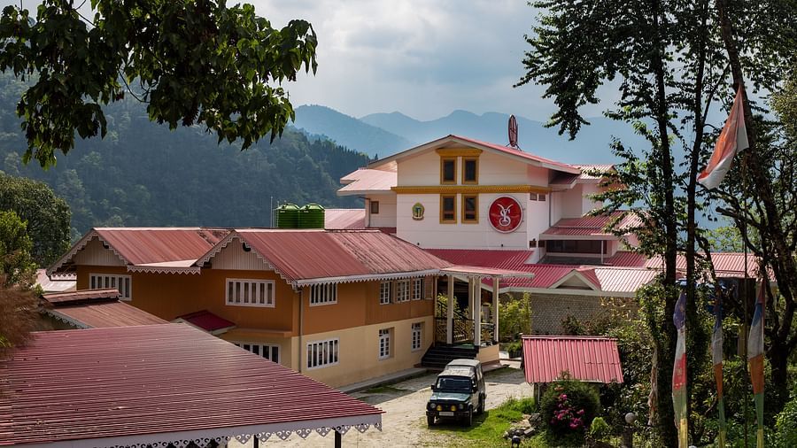 Charming hillside buildings with red rooftops set against a backdrop of lush green mountains under a partly cloudy sky - Yashshree Pelling Chekhim Retreat.