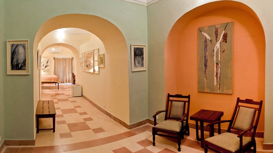 A hallway with arched doorways, framed artwork on the walls, two armchairs, and patterned floor tiles, highlighting the fort-palace's architectural details - Tijara Fort-Palace - 19th Century, Alwar.
