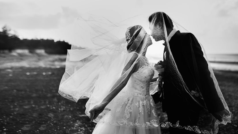A black and white image of a couple going for a kiss with a scenic backdrop