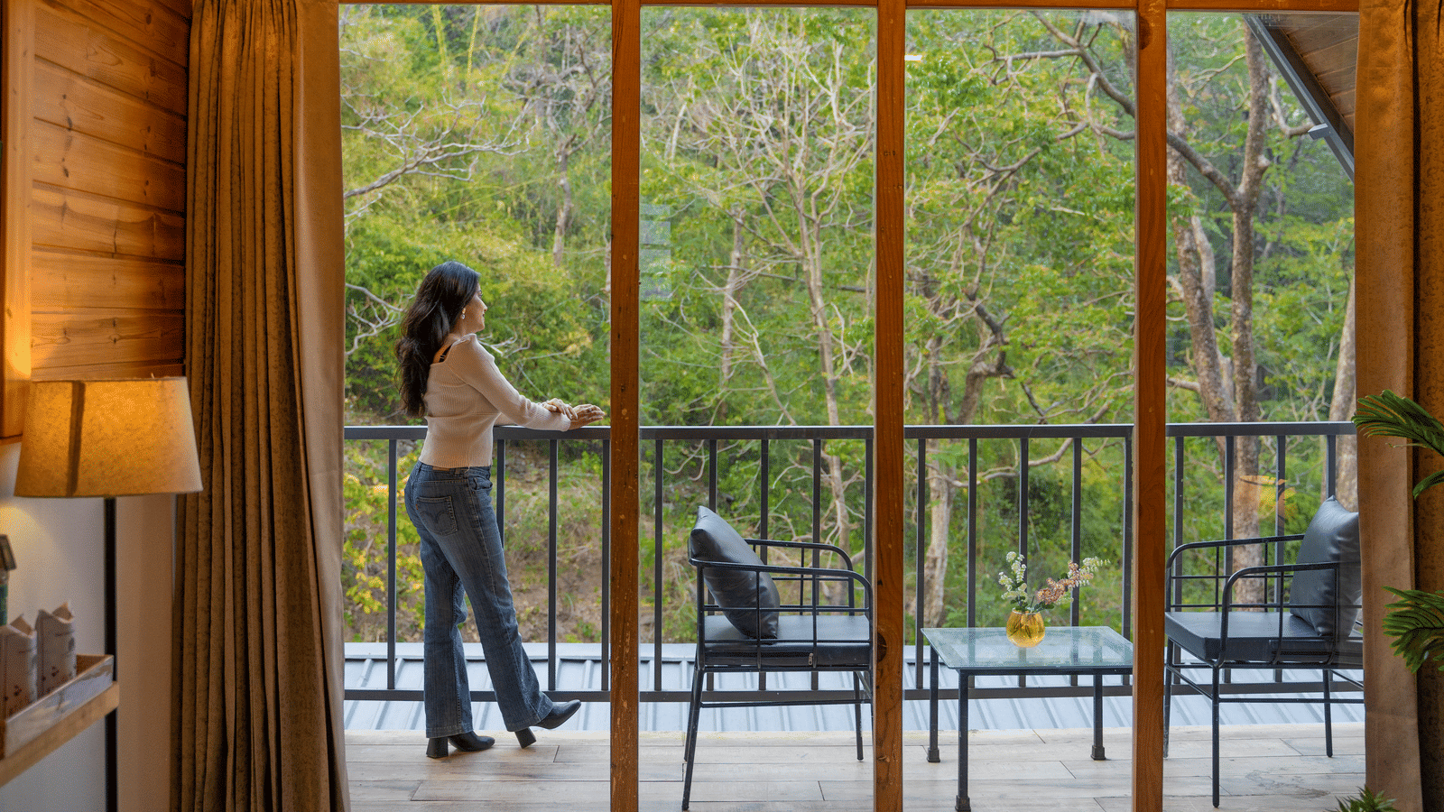 A person stands on a balcony at Perfect Stayz The Jungle Resort, looking at the forest.