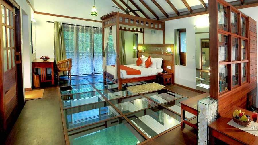 A full view of a glass-floored room that has a bed and other wooden furnishings | Vythiri Resort. Wayanad