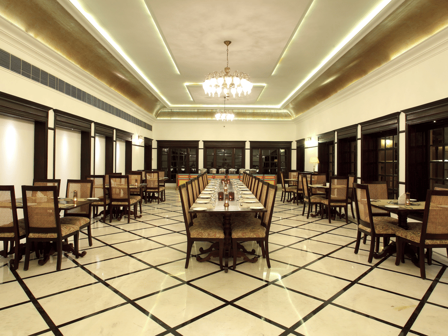 Restaurant at Juna Mahal, Ranthambore featuring several sets of tables and chairs in a spacious dining space.