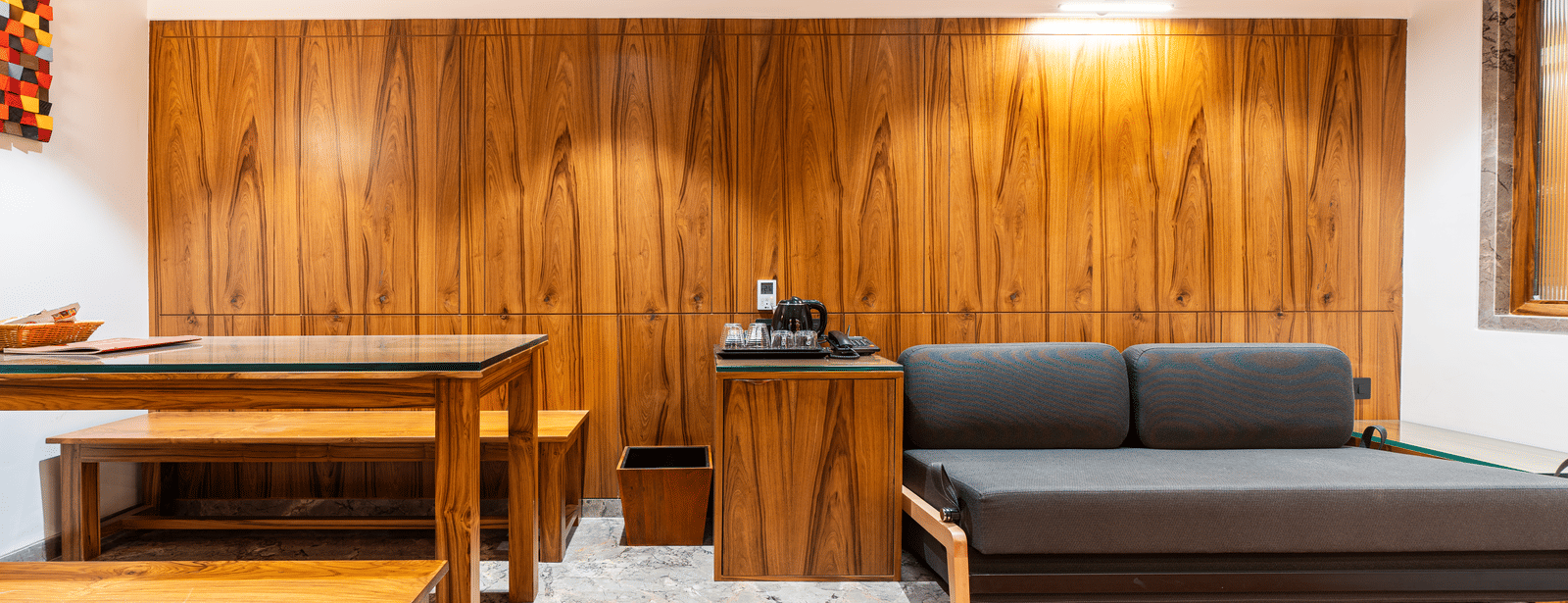 A suite with wooden interiors, dining table, sofa and wall-mounted light at Infiniti Hotel, Indore.