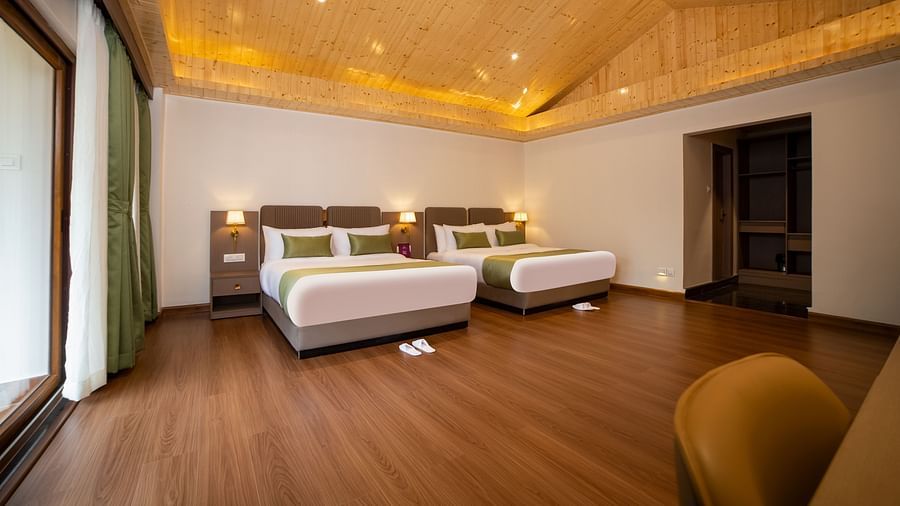 Spacious hotel room with two large beds featuring green accent pillows, wooden flooring and ceiling with recessed lighting, a large window with green curtains, and minimalistic modern furniture - Yashshree Pelling Chekhim Retreat.