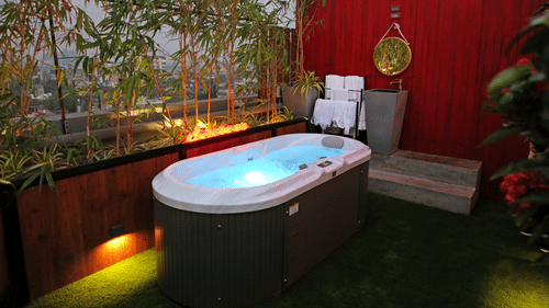 An outdoor jacuzzi on a terrace, under the open night sky, surrounded by well-lit ambience