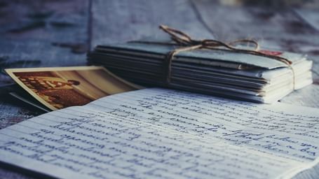 A stack of letters tied with a thin rope placed on an open letter with a vintage postcard beside it.