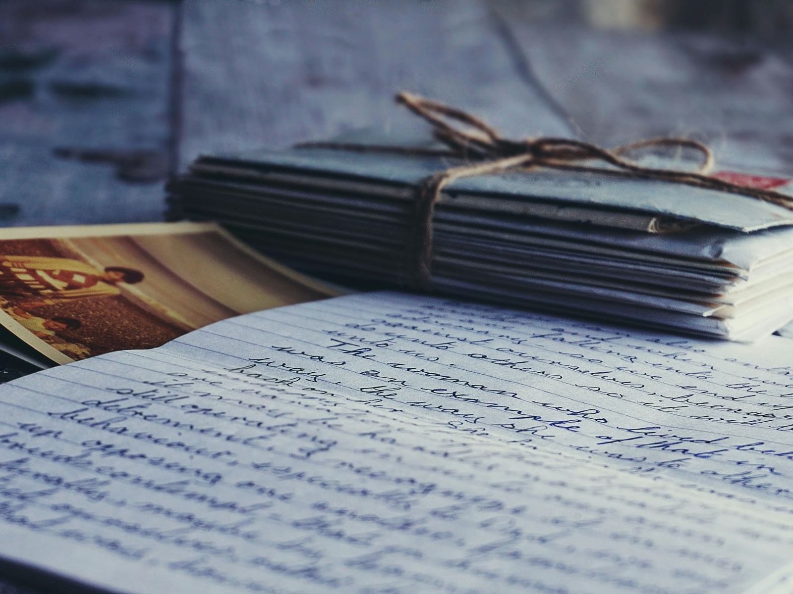 A stack of letters tied with a thin rope placed on an open letter with a vintage postcard beside it.