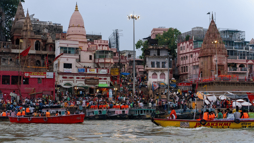 A crowded scene on the Ganges River with boats carrying devotees, against the backdrop of the holy city of Varanasi, India.