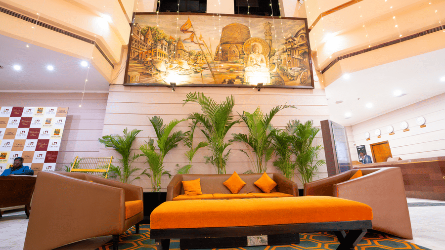 A hotel lobby area with orange and brown sofas, potted plants, and a wall mural | HHI Varanasi