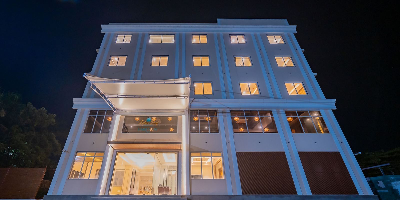 A night view of a modern multi-storey hotel building, brightly lit with warm lights emanating from the windows and entrance at Lotus Leaf Boutique Hotel.
