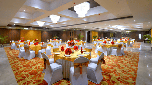 An image of the Royal Ballroom in Agra with chairs placed around round tables and chandeliers hanging from the ceiling - Golden Tulip, Agra