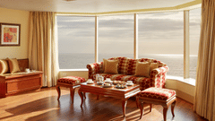 Elegant hotel lounge with a sea view, featuring a red and gold polka-dot sofa set, wooden coffee table with high tea setup, and floor-to-ceiling windows - Ramada Plaza by Wyndham Palm Grove