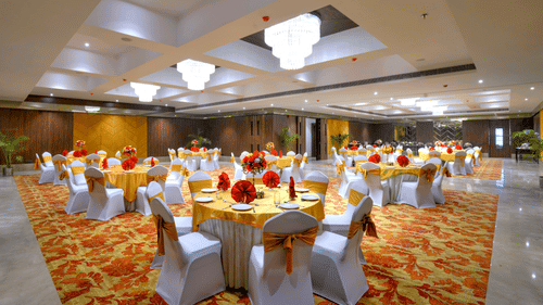 An image of the Royal Ballroom in Agra with chairs placed around round tables and chandeliers hanging from the ceiling - Golden Tulip, Agra