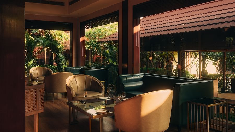 A lounge area at The Ananta Udaipur, featuring comfortable seating, wooden furniture, and  overlooking the lush greenery.
