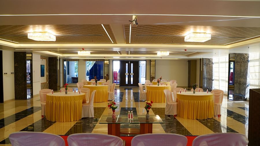 A vibrant event space at BNGV Grandeur Hotel and Banquets, featuring round tables with yellow coverings and red chairs, under warm lighting.