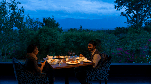 A couple enjoying a romantic meal outdoors in the evening with candlelight at The Serai Bandipur.
