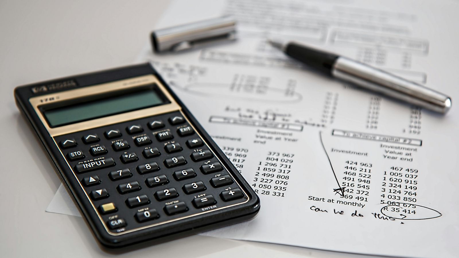 A calculator, pen, and financial documents spread on a desk.